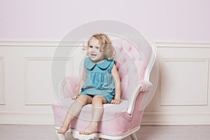 Little beautiful and happy baby girl sitting on a beautiful vintage pink chair in retro dress