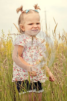 Little beautiful happy girl in everyday clothes. Smiling in a yellow field. With ponytails on their heads. Vertical