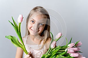 Little beautiful happy girl holding bunch of pink, green tulips in hands. Bouquet, congratulations to the holiday of mother,