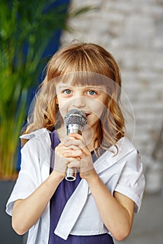A little beautiful kid sings a song in a microphone. The concept