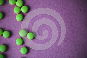 Little beautiful medical pharmaceptic round green pills, vitamins, drugs, antibiotics on a violet pink background, texture.