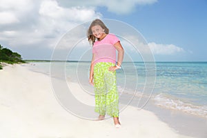 Little beautiful pretty fashionable girl standing on Cuban beach against turquoise ocean and blue sky background