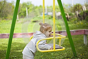 Little beautiful red-haired girl hung on a swing, baby plays on a swing on the playground