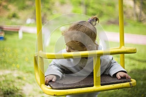 Little beautiful red-haired girl hung on a swing, baby plays on a swing on the playground