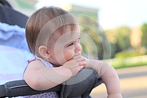 little, beautiful, smiling, cute redhead baby in a pram out-of-doors in a sleeveless shirt holding fingers in his mouth