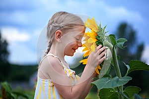 Little beautiful smiling girl in yellow dress in summer day smile in sunflowers field