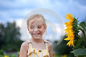 Little beautiful smiling girl in yellow dress in summer day smile in sunflowers field