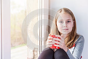 Little beauty girl with cup at the window