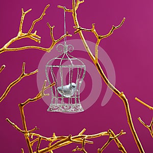 Little bird closed in the silver birdcage hanging on a  golden branches on purple color  background. Freedom concept