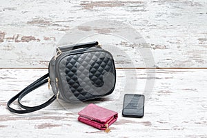 Little black ladies handbag, pink purse and smart phone on wooden background. Fashion concept