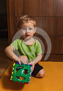 Little blond boy with a big colored figured cube in the hands sat on the floor