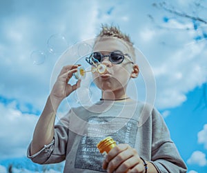 Little Blond Boy Blowing Out Bubbles At Park. Concept of Happy Family And Childhood