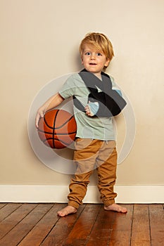 Little blond boy with broken hand holding basketball ball