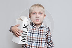 Little blond boy cuddles a large white carton milk package. Light background