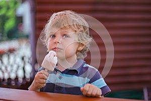 Little blond boy eating yellow ice cream