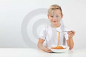 Little blond boy eats spaghetti and smiles