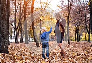 Little blond boy gives his pregnant mother yellow leaf. Autumn park on the background