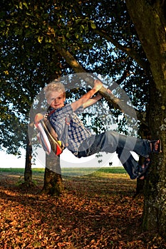 Little blond boy is hanging on the tree with schoolbag