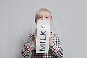 Little blond boy is holding a big white carton milk package. Light background