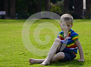 A little blond boy lies sitting on the bright green grass. Space for text