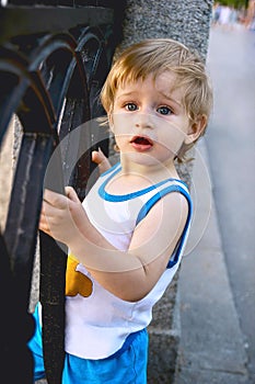 Little blond boy looked with amazement holding on to a cast iron fencing