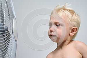 Little blond boy looks at a fan suspiciously. Summer concept