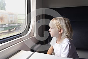 Little blond boy looks thoughtfully out the train window. Rail travel with children
