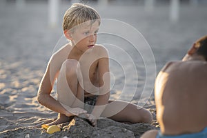 Little blond boy playing with friend on the beach summertime