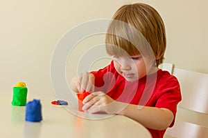 little blond boy playing with plasticine while sitting at table. childhood, developing activities for children