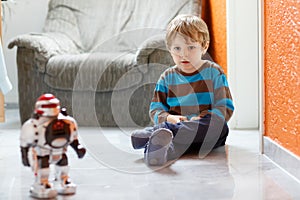 Little blond boy playing with robot toy at home, indoor.