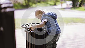 Little blond boy playing with trash in the park.