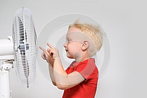 Little blond boy in a red t-shirt touches the fan with his finger. Summer concept