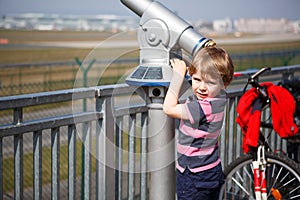 Little blond boy watching airplanes in observation tube on airport