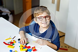 Little blond child with eye glasses playing with lots of colorful plastic blocks.