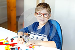 Little blond child with eye glasses playing with lots of colorful plastic blocks.