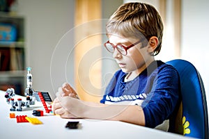 Little blond child with eye glasses playing with lots of colorful plastic blocks. Adorable school kid boy having fun