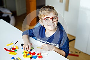 Little blond child with eye glasses playing with lots of colorful plastic blocks. Adorable school kid boy having fun