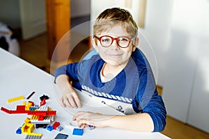 Little blond child with eye glasses playing with lots of colorful plastic blocks. Adorable school kid boy having fun