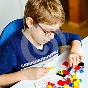 Little blond child with eye glasses playing with lots of colorful plastic blocks. Adorable school kid boy having fun