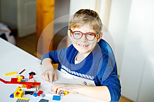 Little blond child with eye glasses playing with lots of colorful plastic blocks. Adorable school kid boy having fun