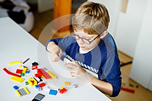 Little blond child with eye glasses playing with lots of colorful plastic blocks. Adorable school kid boy having fun