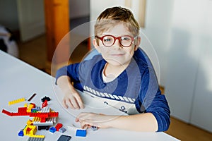 Little blond child with eye glasses playing with lots of colorful plastic blocks. Adorable school kid boy having fun