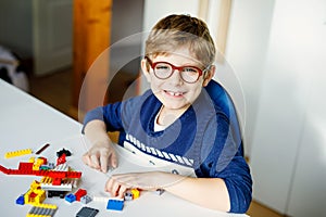 Little blond child with eye glasses playing with lots of colorful plastic blocks. Adorable school kid boy having fun