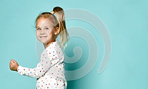 Little blond child in a heart-shaped print shirt. She smiles, fools around, has fun against the backdrop of a mint studio