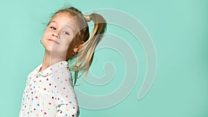 Little blond child in a heart-shaped print shirt. She smiles, fools around, has fun against the backdrop of a mint studio