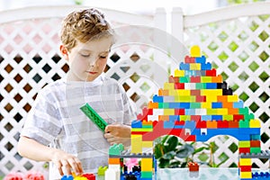 Little blond child and kid boy playing with lots of colorful plastic blocks.