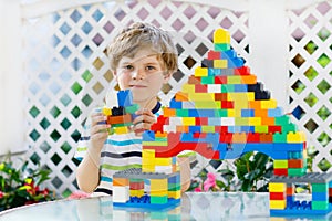 Little blond child and kid boy playing with lots of colorful plastic blocks.