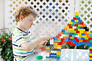 Little blond child and kid boy playing with lots of colorful plastic blocks.