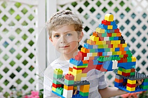 Little blond child and kid boy playing with lots of colorful plastic blocks.