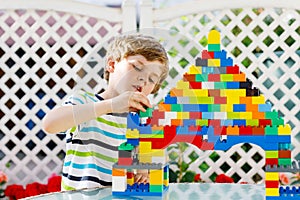 Little blond child and kid boy playing with lots of colorful plastic blocks.